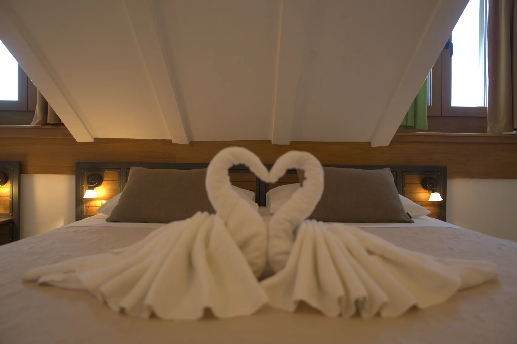 The bed beneath the white beams of the sloping ceiling, with towels folded into swans, Hotel Villa Diana, Lučac, Split